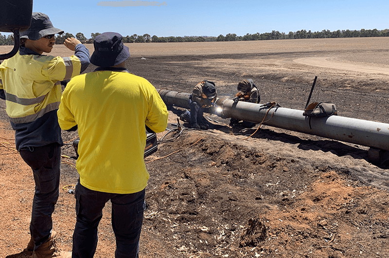 Two Water Corporation crew members watching a colleague fix a damaged water pipe